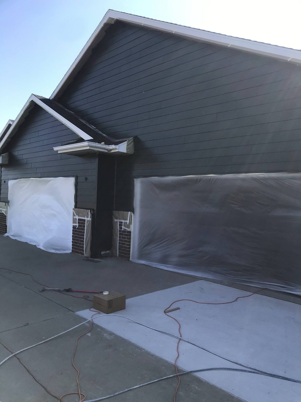 House exterior masked off with plastic sheeting and drop cloths, prepped for spraying