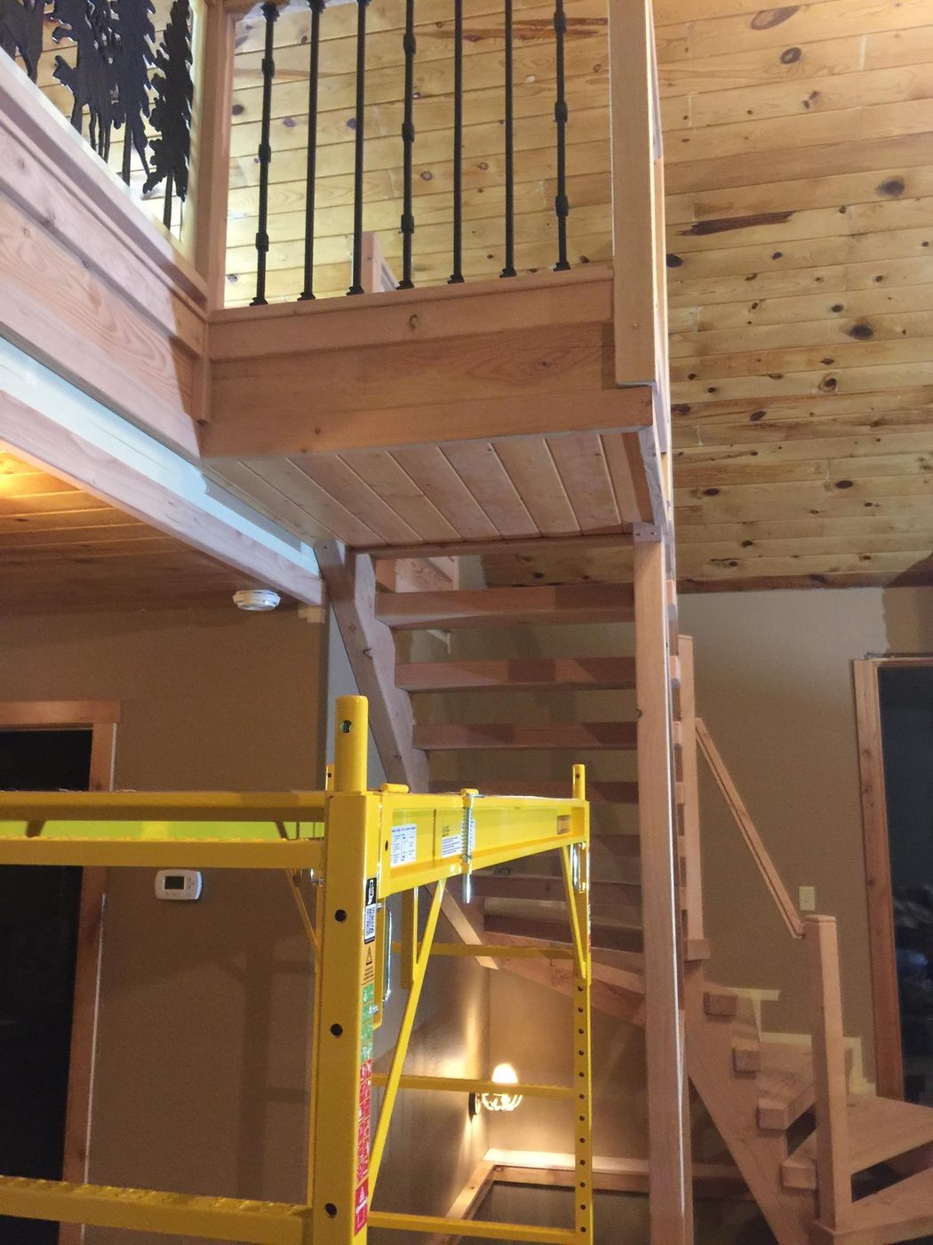 Interior stairwell with pine ceiling and railings, scaffolding set up mid-project